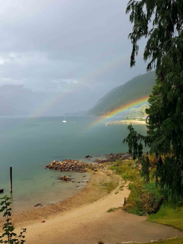 A rainbow over the water and trees on the shore.